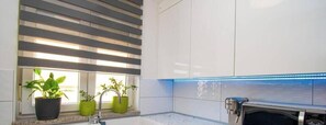 A modern kitchen with a built-in oven, a window with blinds, and potted plants on the windowsill. - Luka Apartment, Pula (Marčana)