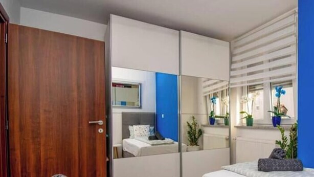 Una camera da letto con un letto, un armadio, uno specchio e una finestra con piante.