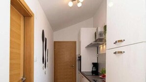 A narrow hallway with a wooden door, a white wall, and a kitchen area with cabinets and a stove. - Megy Apartment with Ocean View, Medulin (Marčana)