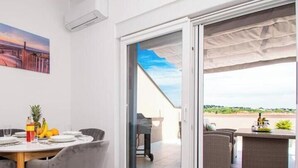 A dining area with a table set for two, a painting on the wall, and a sliding glass door leading to an outdoor patio. - Megy Apartment with Ocean View, Medulin (Marčana)