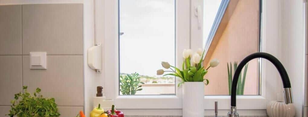 A bathroom with a window, a white vase with flowers, a black faucet, and a white soap dispenser.