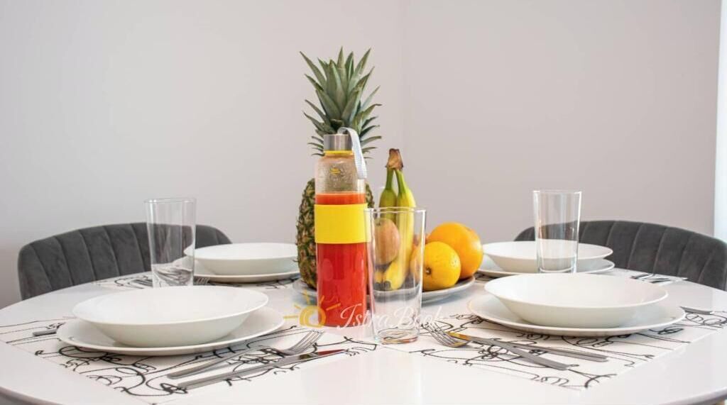 Een eettafel gedekt met borden, bestek, een fruitschaal en glazen.