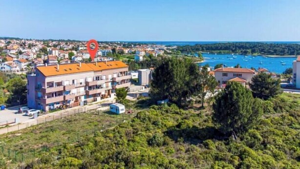 Uma área residencial costeira com um prédio vermelho notável, provavelmente um hotel, com vários andares e varandas.