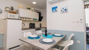 Cozinha compacta com armários brancos, micro-ondas e cafeteira. Há uma mesa de jantar com cadeiras e um jogo americano azul.