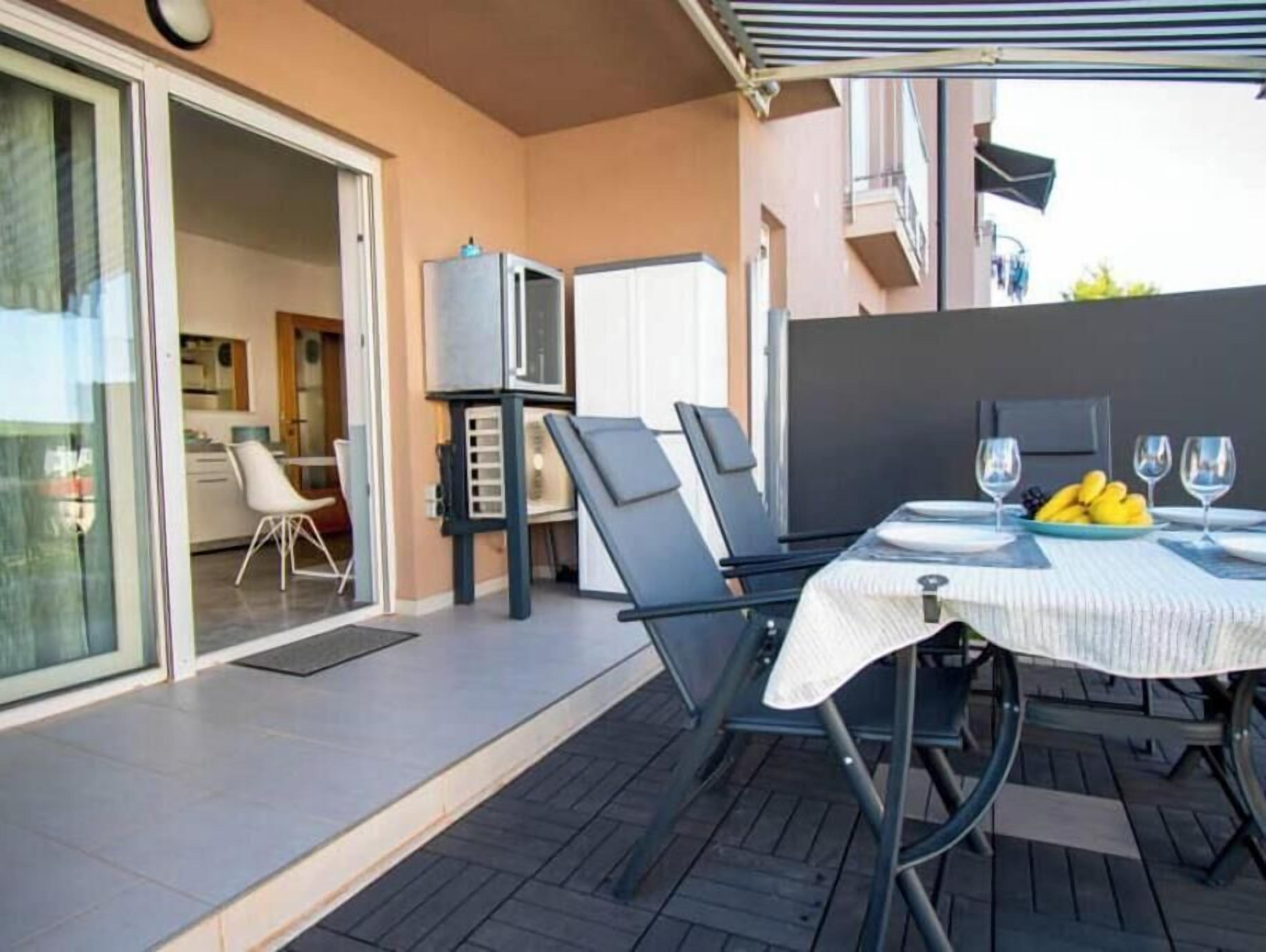 Una zona d'esbarjo exterior amb taula per a dos, una barbacoa i una porta corredissa de vidre que dona a una cuina.