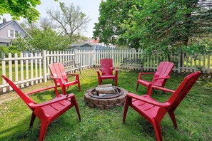 A backyard with a fire pit, red Adirondack chairs, and a white picket fence. - The Darling Duplex North Apartment 6 guests. 2 bedrooms. 1.5 bathrooms. (South Haven)