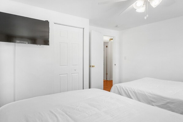 A bedroom with two beds, a TV mounted on the wall, and a ceiling fan.
