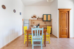 A dining area with a table and chairs, a kitchen in the background, and a wooden door. - Domus Maris Felloniche by BarbaHouse (Castrignano del Capo)