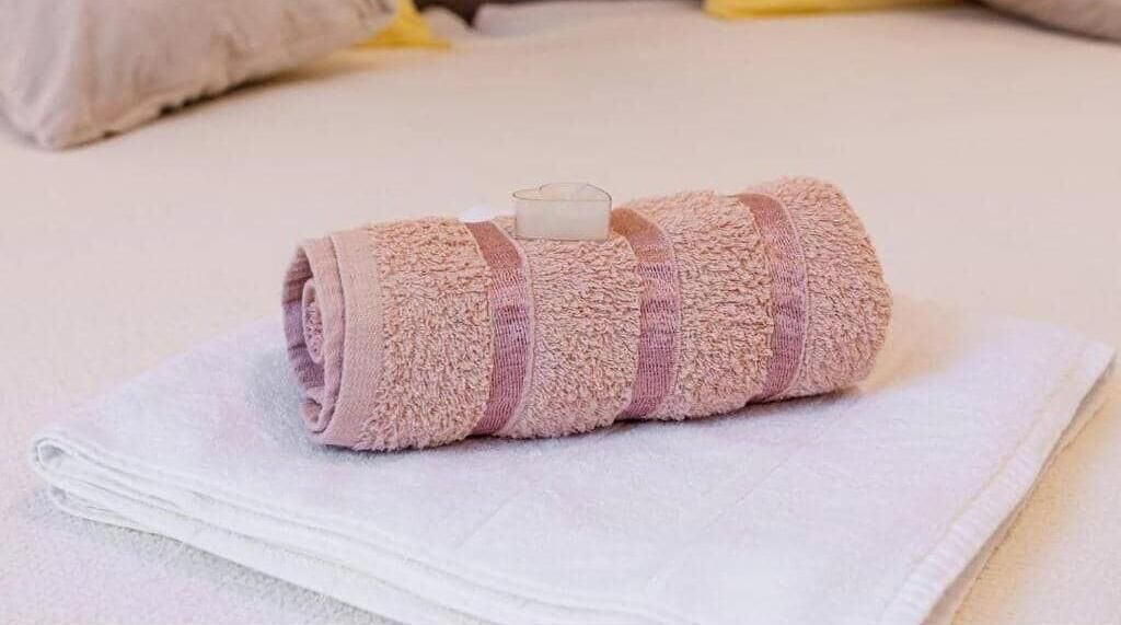 Una toalla enrollada sobre la cama, con otra toalla blanca debajo.