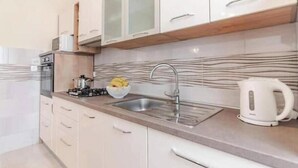 Een keuken met een gasfornuis, spoelbak en waterkoker. Er zijn kastjes en een aanrecht.