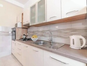 A kitchen with a gas stove, sink, and a kettle. There are cabinets and a countertop. - Apartment Stella, Medulin (Marčana)