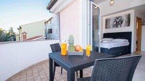 Een balkon met een tafel gedekt voor twee personen, een bed met hoofdbord en een schilderij aan de muur.