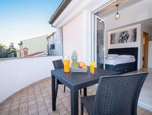 A balcony with a table set for two, a bed with a headboard, and a painting on the wall. - Apartment Sun, Pula (Marčana)