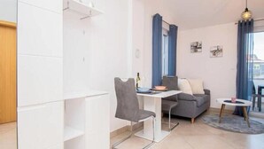 Een moderne woonkamer met een eetgedeelte, een grijze bank, een kleine ronde tafel en een raam met gordijnen.