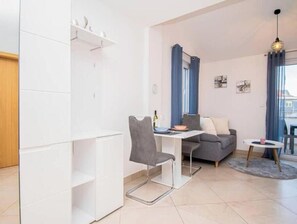A modern living room with a dining area, a grey sofa, a small round table, and a window with curtains. - Apartment Sun, Pula (Marčana)
