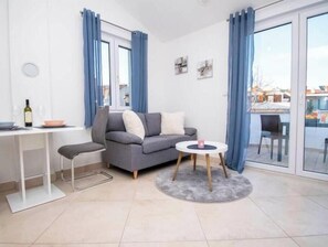 A modern living room with a grey sofa, a small round table, a dining table with chairs, and a glass door leading to an outdoor area. - Apartment Sun, Pula (Marčana)