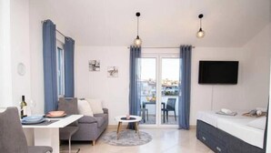 Een moderne woonkamer met een bank, een eettafel en een aan de muur bevestigde televisie.