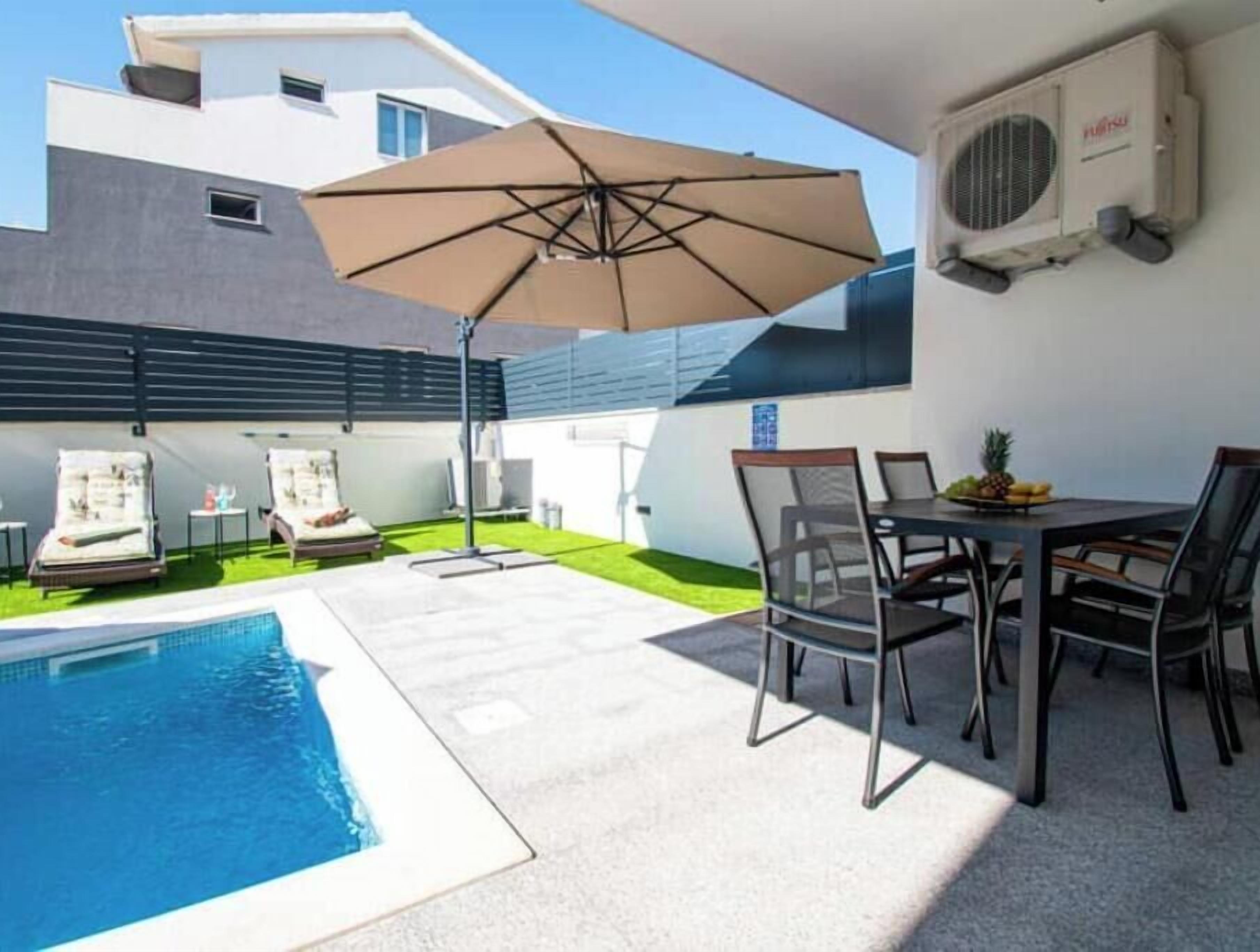 Un espace piscine aménagé avec des chaises longues, une table à manger et un parasol.