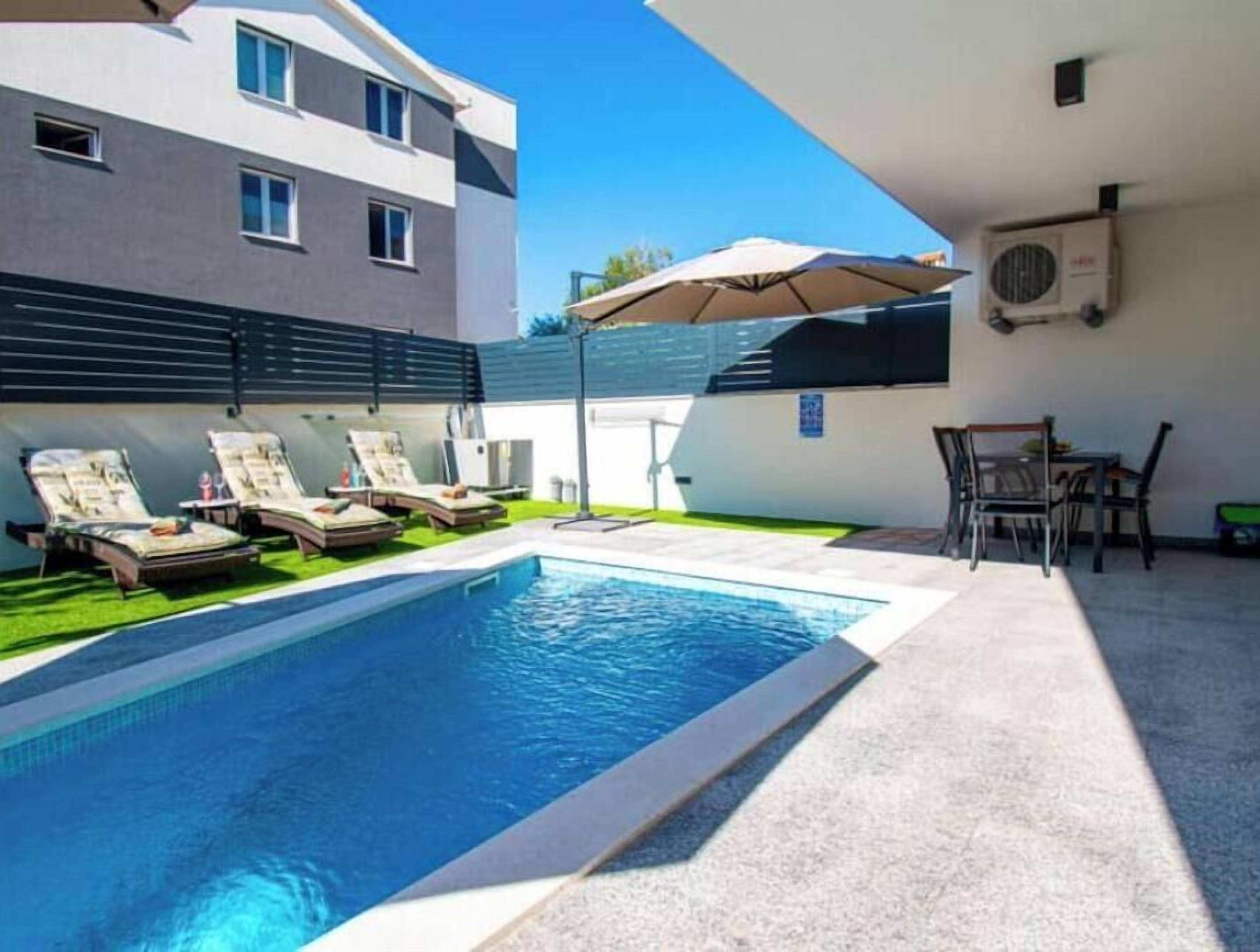 A swimming pool with lounge chairs, a table, and an umbrella.