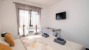 Un dormitorio con cama, escritorio, televisor y ventana con cortinas.