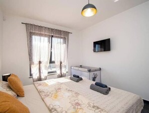 Ein Schlafzimmer mit einem Bett, einem Schreibtisch, einem Fernseher und einem Fenster mit Vorhängen.
