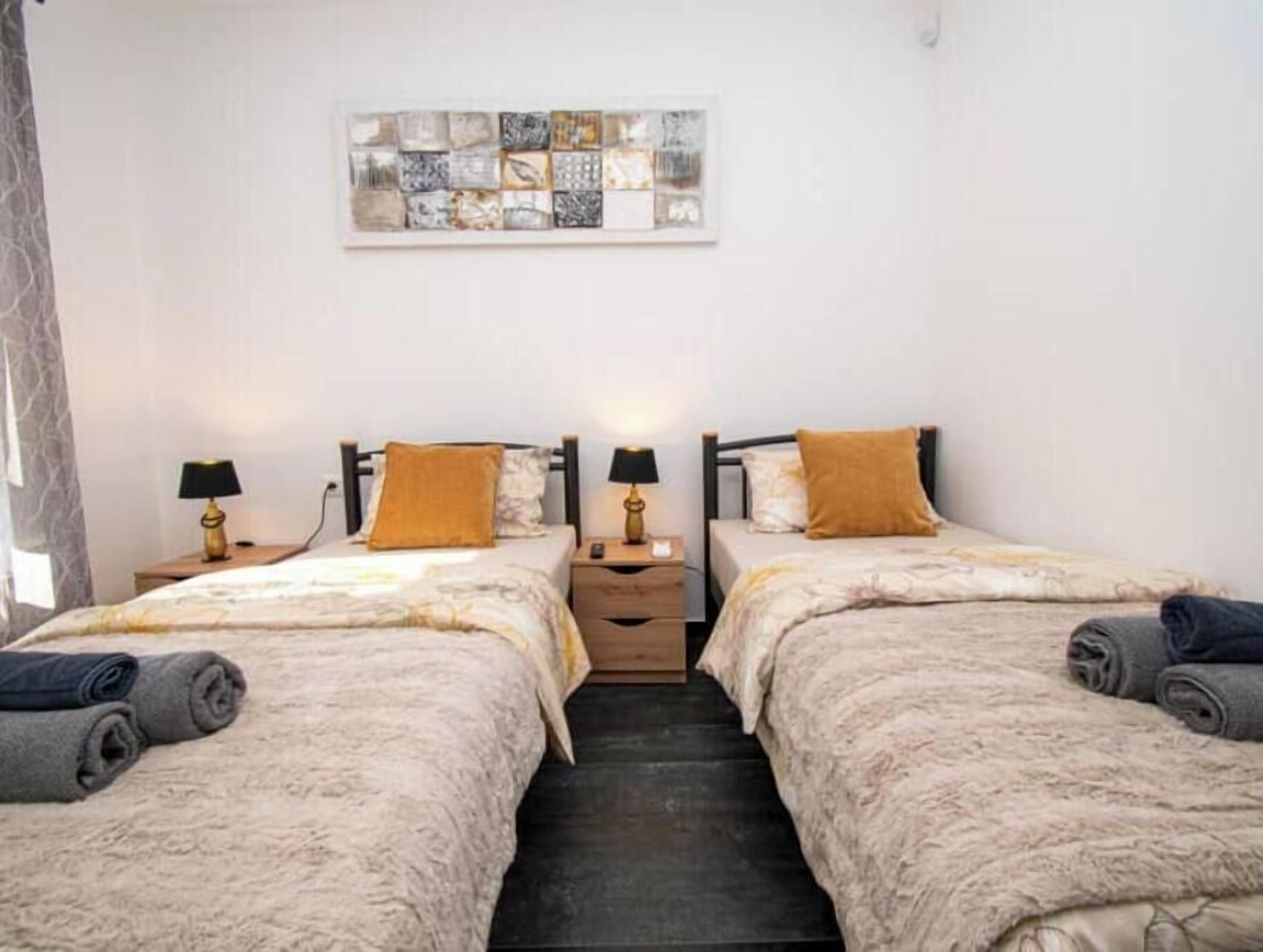 A double room with two beds, each with a lamp and a pillow. There is a small table between the beds.