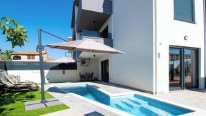 Un edificio moderno con piscina, asientos exteriores y un patio cubierto.
