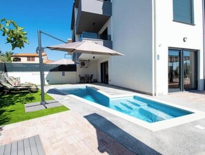 Ein modernes Gebäude mit Schwimmbad, Sitzgelegenheiten im Freien und einer überdachten Terrassenfläche.