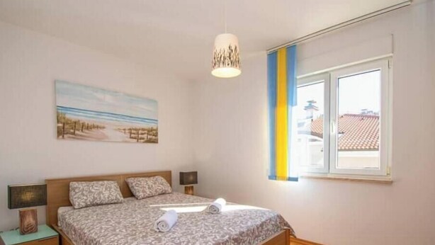 Ett sovrum med en säng, sängbord, en tavla, ett fönster med persienner och en hängande lampa.