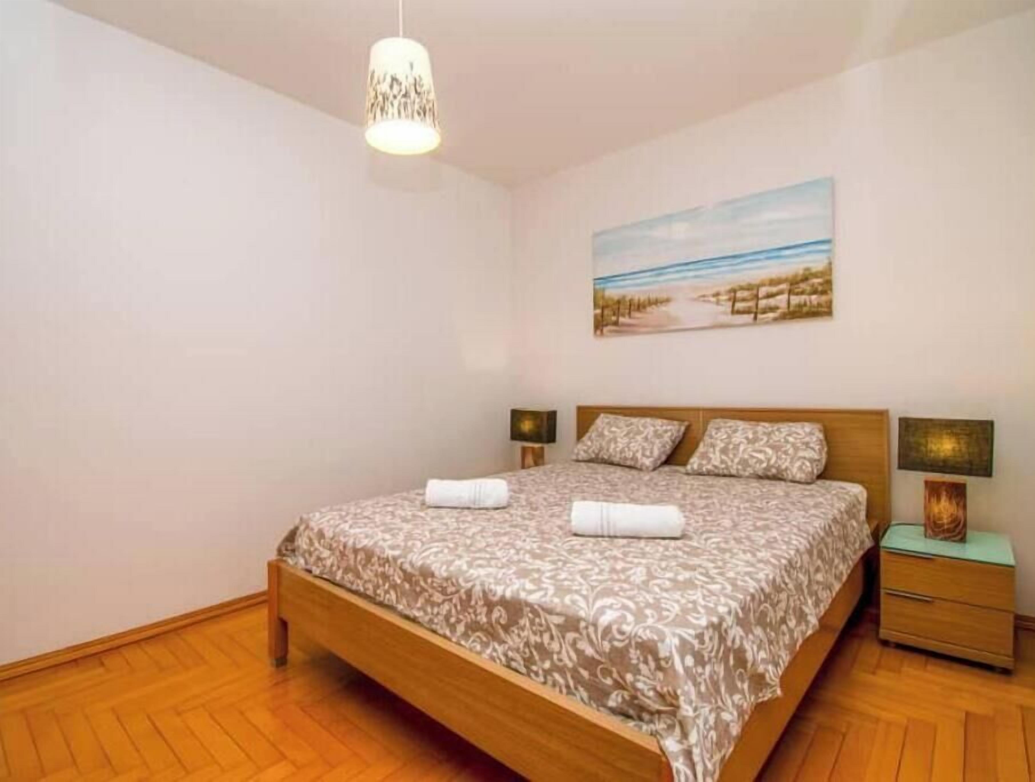Un dormitorio con una cama de madera, dos lámparas de noche, un cuadro en la pared y una lámpara colgante.