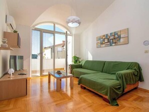 A modern living room with a wooden floor, a green sofa, a glass coffee table, and a large window with a view. - Vallis Apartment, Pula (Marčana)