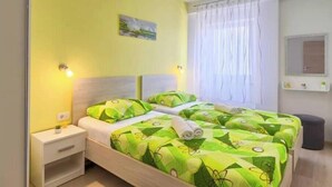 A double bed with green patterned bedding, a bedside table, a nightstand, a window with white curtains, and a small mirror on the wall. - Apartment Viola, Medulin (Marčana)