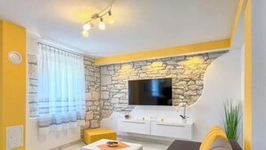 A living room with a stone wall, a flat-screen TV, a sofa, a coffee table, and a window with curtains. - Apartment Viola, Medulin (Marčana)
