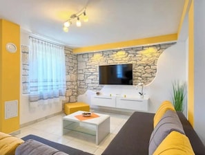 Ein Wohnzimmer mit Steinsandsteinwand, einem Flachbildfernseher, einer Couch, einem Couchtisch und einem Fenster mit Vorhängen.