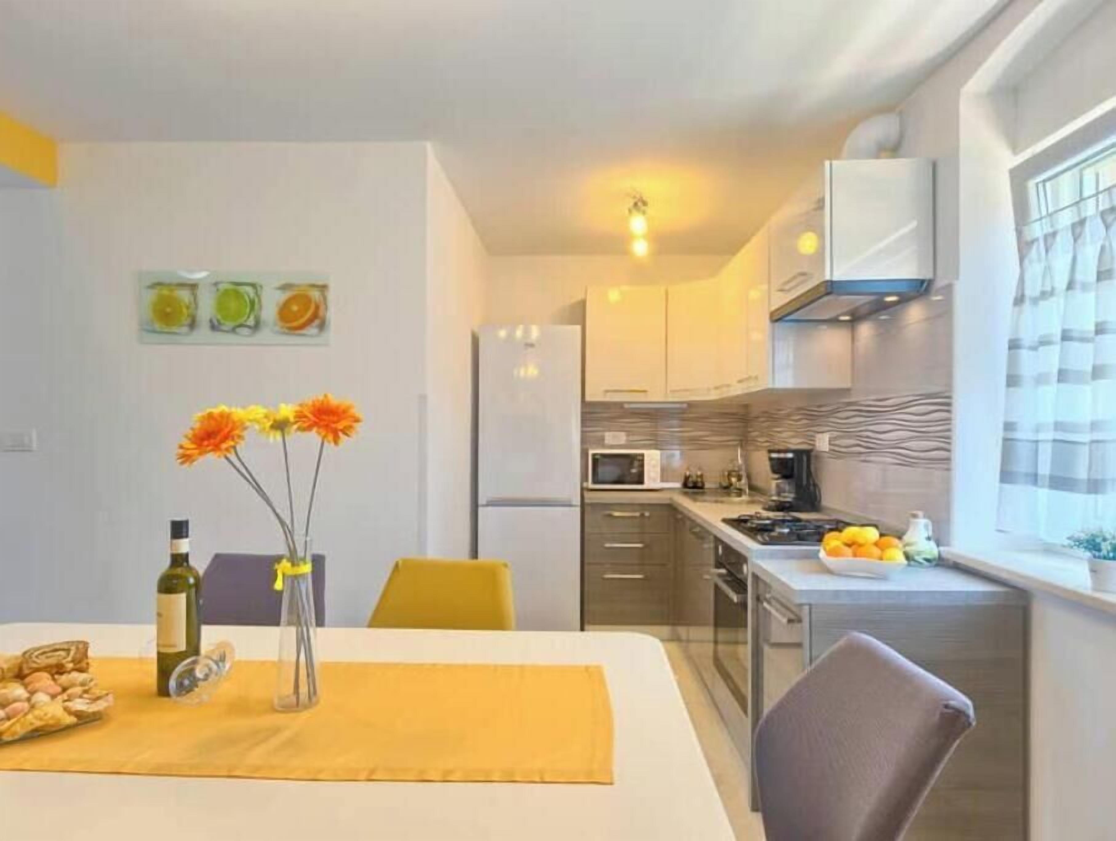Une cuisine compacte dotée d’appareils électroménagers modernes, un coin repas avec une table dressée pour deux personnes, et une fenêtre avec des rideaux.