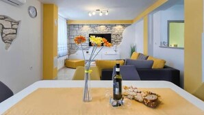 A modern living room with a stone wall, a dining table with a bottle and glasses, and a sofa with cushions. - Apartment Viola, Medulin (Marčana)