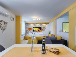 Ein modernes Wohnzimmer mit Steinwand, einem Esstisch mit Flasche und Gläsern sowie einer Couch mit Kissen.