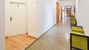 Un pasillo con puertas numeradas, suelo alfombrado y una zona de estar con sillas amarillas.