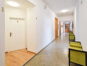Ein Korridor mit nummerierten Türen, einem Teppichboden und einer Sitzecke mit gelben Stühlen.