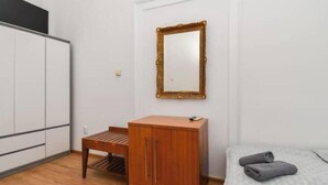 Un dormitorio con cama, cómoda de madera, una mesita y un espejo en la pared.