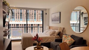 Un soggiorno moderno con un letto, un divano, un tavolo da pranzo e una grande finestra che offre vista sugli edifici.