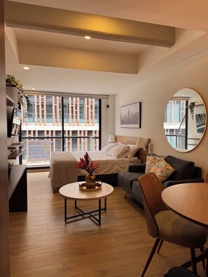 Ein modernes Wohnzimmer mit einem Bett, einem Sofa, einem Esstisch und einem großen Fenster mit Blick auf Gebäude.