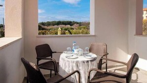 A balcony with a round table and four wicker chairs, overlooking a landscape with trees and a clear sky. - A01 - C: Lotus Apartment (Marčana)
