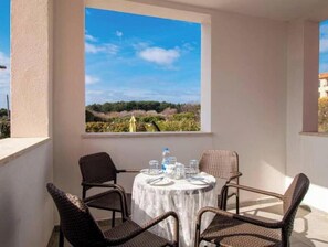 A balcony with a round table and four wicker chairs, overlooking a landscape with trees and a clear sky. - A01 - C: Lotus Apartment (Marčana)