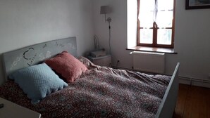 Un dormitorio con cama, mesita de noche, lámpara, ventana y radiador.