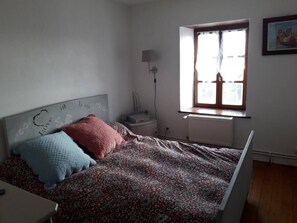 Ein Schlafzimmer mit einem Bett, einem Nachttisch, einer Lampe, einem Fenster und einer Heizung.