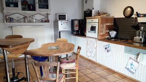 A kitchen with a dining table, chairs, a microwave, refrigerator, and a coffee machine. - House surrounded by nature, Entire home in Palladuc, France (Palladuc)