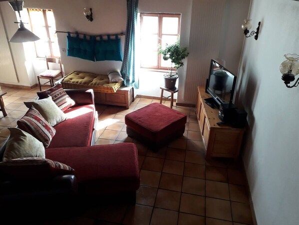 Ein Wohnzimmer mit Sofa, Hocker, Fernseher und einer Topfpflanze.