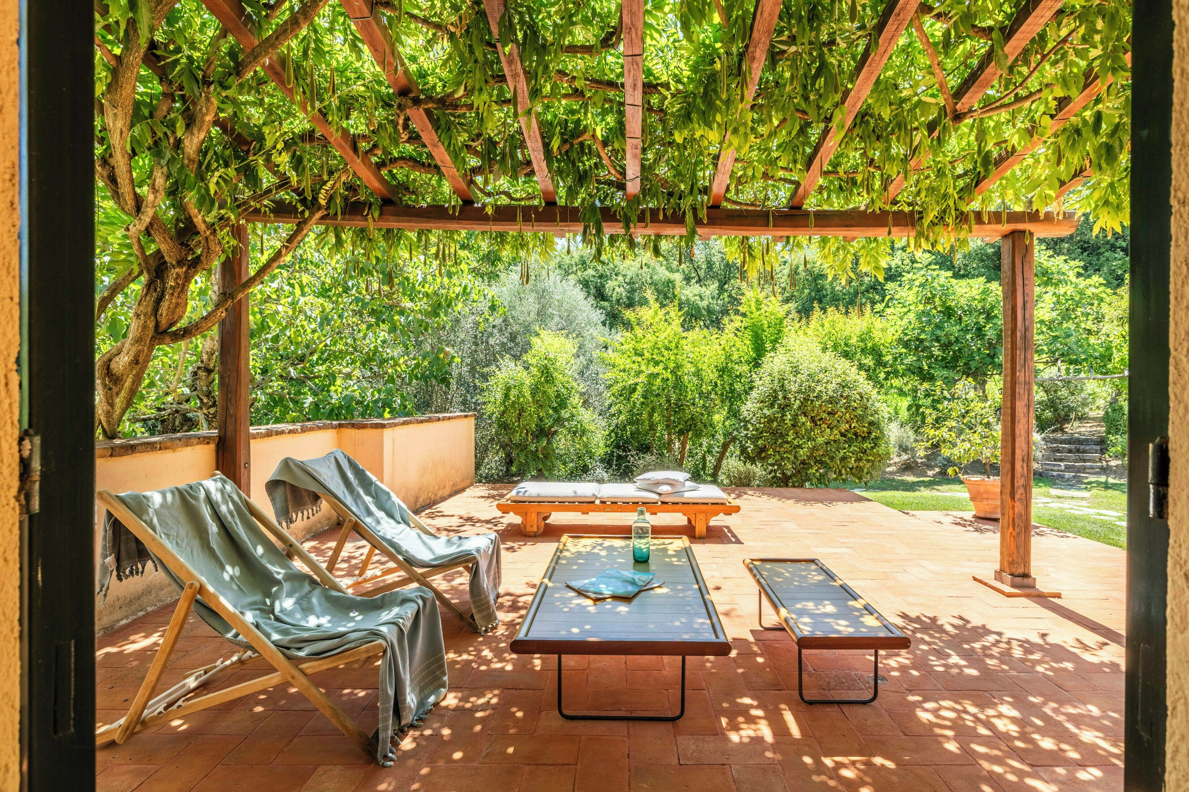 En uteplats med en pergola, solstolar, ett bord och en bänk.