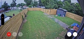 A fenced backyard with a grassy area, a small shed, and a blue tarp on the ground.